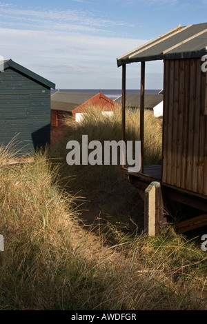 Hölzerne Strandhütten liegen unter hohen grasbewachsenen Sanddünen am Strand von Norfolk Stockfoto