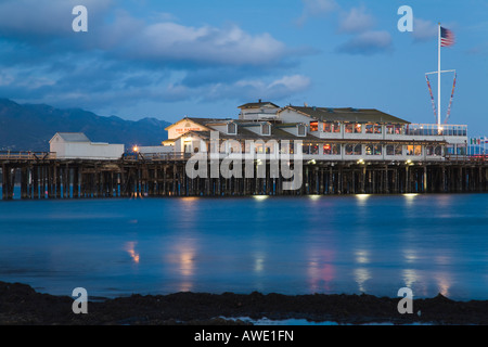 CALIFORNIA Santa Barbara Stearns Wharf Pier erstrecken sich in den Pazifischen Ozean Restaurants und Shops at Dusk Gebäude und Flagge Stockfoto