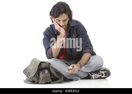 Teenager, der mit gekreuzten Beinen sitzt und eine Wählnummer anwählt Mobiltelefon Stockfoto