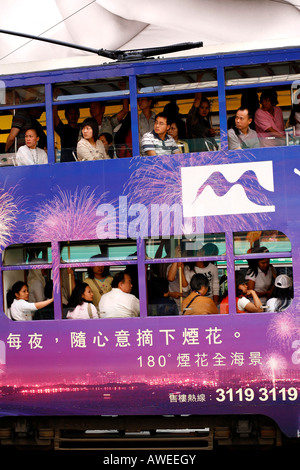 Die Passagiere an Bord eines doppelstöckigen Straßenbahn Bus mit Werbung in Hongkong, China Stockfoto