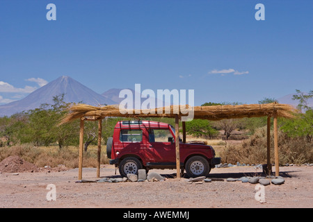 Geländewagen, der unter Sonnenschutz vor einem kleinen Lehmhaus steht, im Hintergrund der Vulkan Licancabur, San Pedro de Stockfoto