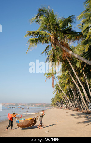 Mui Ne Beach-Szene mit zwei Fischer tragen ihre Corracle Boot aus dem Meer Stockfoto