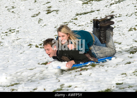 Mann mit einer Frau auf dem Rücken, liegend auf einem Schlitten, Schlitten, auf einem Hügel hinunter, Ehemann Frau, Spaß Stockfoto