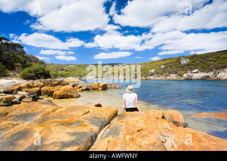 Eine junge Frau saß auf Granitfelsen neben dem Waychinicup Fluss Einlass im Waychinicup National Park in der Nähe von Albany, Westaustralien Stockfoto