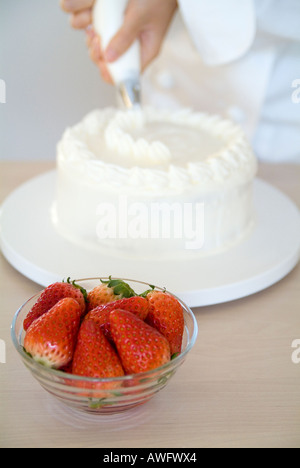 Eine Frau, die einen Kuchen mit Schlagsahne verzieren Stockfoto
