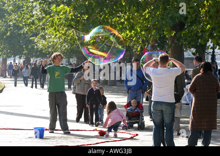 A Street Performer bläst riesige Seifenblasen um Touristen und Kinder in der Nähe von London Eye auf der Themse London England UK EU unterhalten Stockfoto