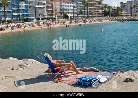 Reife Frau Sonnen auf einem Pier, Juan Les Pins, Côte d ' Azur. Überfüllten Strand im Hintergrund. Stockfoto