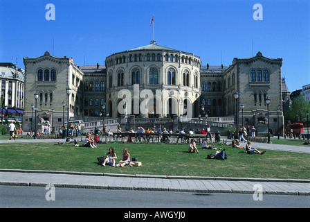 Norwegen, Oslo, Stortinget, Leute sitzen in Gelände, Gebäude, Fassade des Parlaments aus gelbem Backstein gebaut auf rötliche Granitsockel Stockfoto