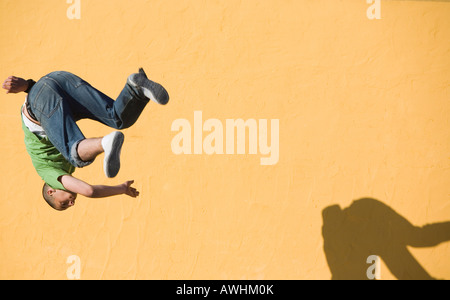 Junger Mann macht einen Salto mit Schatten auf gelbe Wand Stockfoto