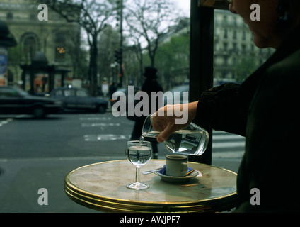 Person sitzt am Tisch auf der Terrasse des Cafés, gießt Wasser aus der Karaffe Stockfoto