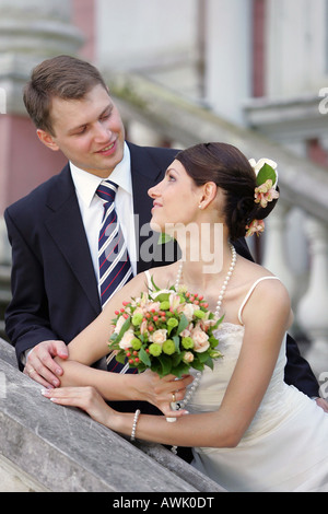 Schöne lächelnde Braut im weißen Kleid am Hochzeitstag. Sie hält einen Blumenstrauß und liebevoll mit Blick auf den Bräutigam Stockfoto