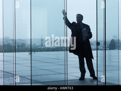 Mann stehend außerhalb Glastüren des Gebäudes Lobby, winken Stockfoto