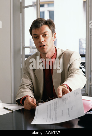 Mann am Schreibtisch sitzt, hält Dokument Stockfoto