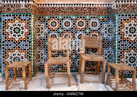Alte Holzstühle und Hocker vor einer schönen gefliesten Wand, Ali-Ben-Youssef madrasah, historische theologische Akademie in der Stockfoto
