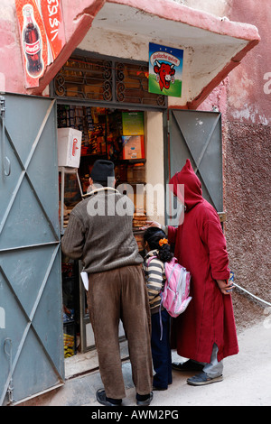 Junges Mädchen Schule Rucksack stehend zwischen zwei Männer vor einem kleinen Gastronomie Kiosk, Marrakesch, Marokko, Afrika Stockfoto