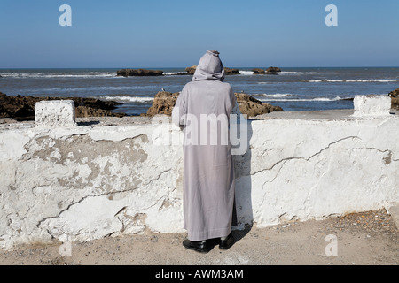 Mann in traditioneller Kleidung über die Hafenwand mit Blick auf das Meer, Essaouira, Marokko, Afrika Stockfoto