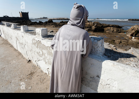 Mann in traditioneller Kleidung über die Hafenwand mit Blick auf das Meer, Essaouira, Marokko, Afrika Stockfoto