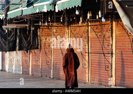 Mann trägt eine Djellaba, vorbei an kleinen geschlossenen Souk-Läden, Djemaa el Fna, Marrakesch, Marokko, Afrika Stockfoto