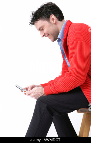 Mann trägt rote Jacke sitzen auf Stuhl, Blick auf sein Handy Stockfoto