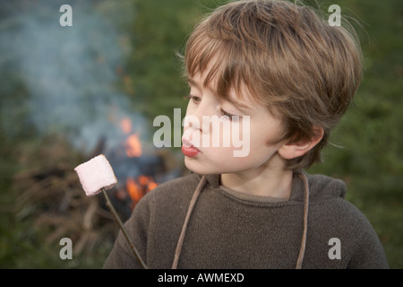 Kind Rösten Marshmallows im Garten außen und bläst darauf zum abkühlen Stockfoto