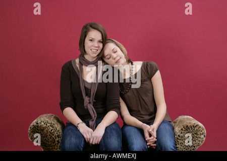 Zwei Mädchen, Pre-Teens, schon als Teenager auf einem Tiger-Print-Sofa kuscheln Stockfoto