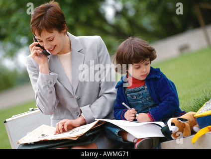 Geschäftsfrau und Kind außerhalb zusammensitzen, Frau mit Handy Stockfoto