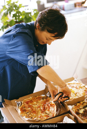 Frau Schnitt Scheiben von Pizza mit Schere, Hüfte aufwärts Stockfoto