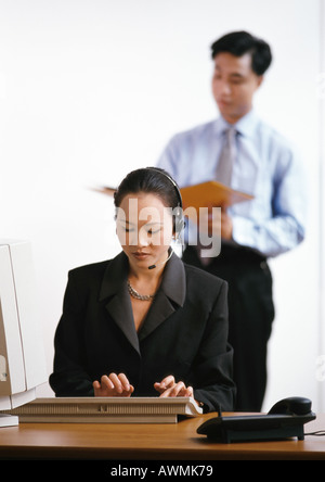 Geschäftsfrau, die Eingabe über Tastatur, Mann im Hintergrund Stockfoto