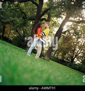 Junger Mann und Frau stehen auf dem Rasen, umarmen, Seitenansicht, in voller Länge Stockfoto