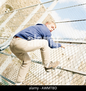 Junger Mann Klettern Maschendrahtzaun. Stockfoto