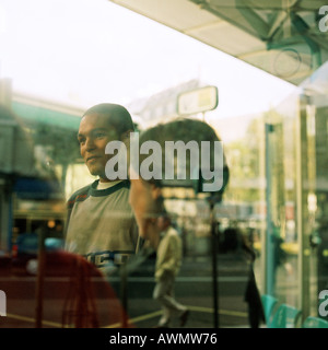 Junge Menschen, die durch Fenster mit Reflexionen, außen am Busbahnhof gesehen Stockfoto