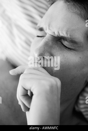 Das Gesicht des Mannes mit den Augen geschlossen und runzelte die Stirn, Hand über Mund, liegend auf dem Bett, close-up, schwarz und weiß. Stockfoto