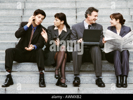 Vier Geschäftsleute sitzen auf Stufen, Interaktion. Stockfoto