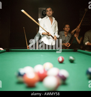 Junger Mann schießen Pool, Leute zu beobachten im Hintergrund, Billard-Kugeln im Vordergrund unscharf Stockfoto