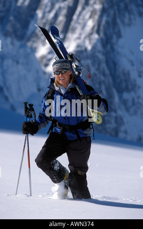 Junge Frau, die zu Fuß durch Schnee mit Skiern auf die Schulter Stockfoto