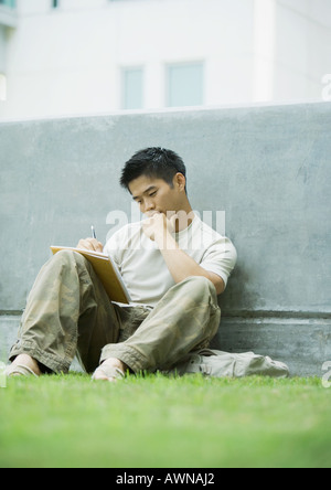 Junger Mann auf dem Rasen sitzen und studieren Stockfoto
