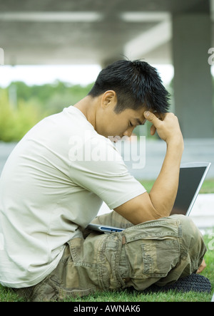 Mann mit Laptop, Gras sitzen Kopf haltend Stockfoto