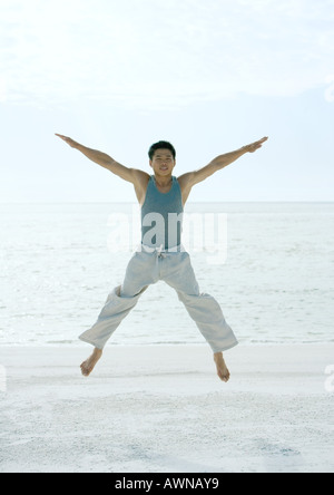 Mann springt gespreizt am Strand Stockfoto