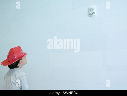 Junge Fireman es Hut, blickte zu Rauchmelder an Wand Stockfoto
