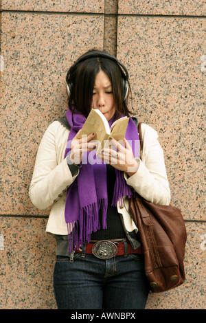 Eine junge Japanerin tragen von Kopfhörern und einem Buch in Tokio, Japan Stockfoto