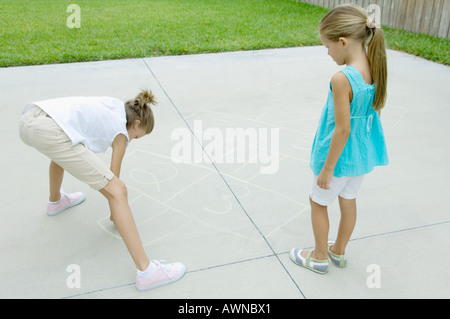 Himmel und Hölle Spiel auf Einfahrt zu zeichnen, während zweite Mädchen wartet Mädchen Stockfoto