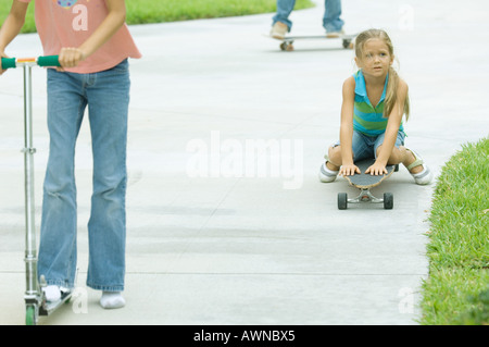 Kinder reiten, Rollern und Skateboards in Einfahrt Stockfoto