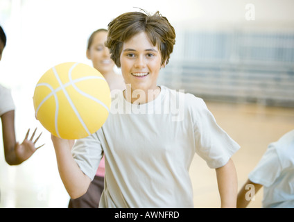 Teenager mit Basketball in Turnhalle, gefolgt von Klassenkameraden Stockfoto