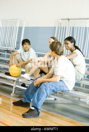 Gruppe von Jugendlichen sitzen mit Basketball auf Tribüne in Turnhalle Stockfoto