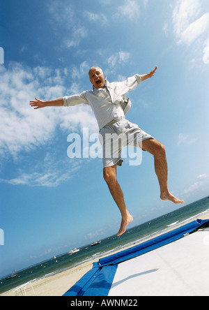 Reifer Mann springen auf dem Trampolin am Strand, Arme, Mund offen Stockfoto