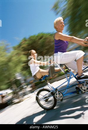 Reife Frau und Mädchen mit Tandem Fahrrad, Granddaugher kleben ihre Beine, verschwommen Stockfoto