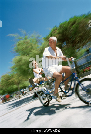 Reifer Mann und Mädchen, die Enkelin mit Beinen heraus, Tandem Fahrrad verschwommen Bewegung Stockfoto