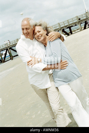 Älteres Paar mit Arme umeinander zu Fuß am Strand Stockfoto