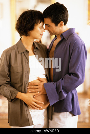 Mann umarmt schwangere Frau, beide Hände auf den Bauch, Porträt Stockfoto