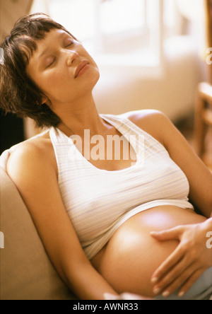Schwangere Frau im Sessel, geschlossenen Augen und Hand auf Bauch Stockfoto